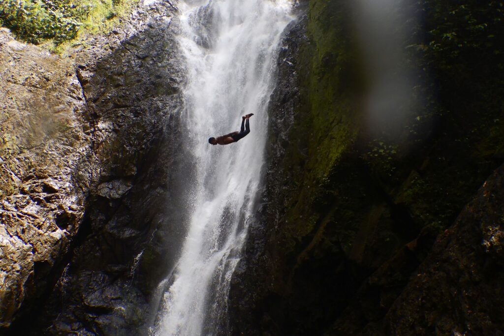 Man jumping off a cliff in front of a waterfall